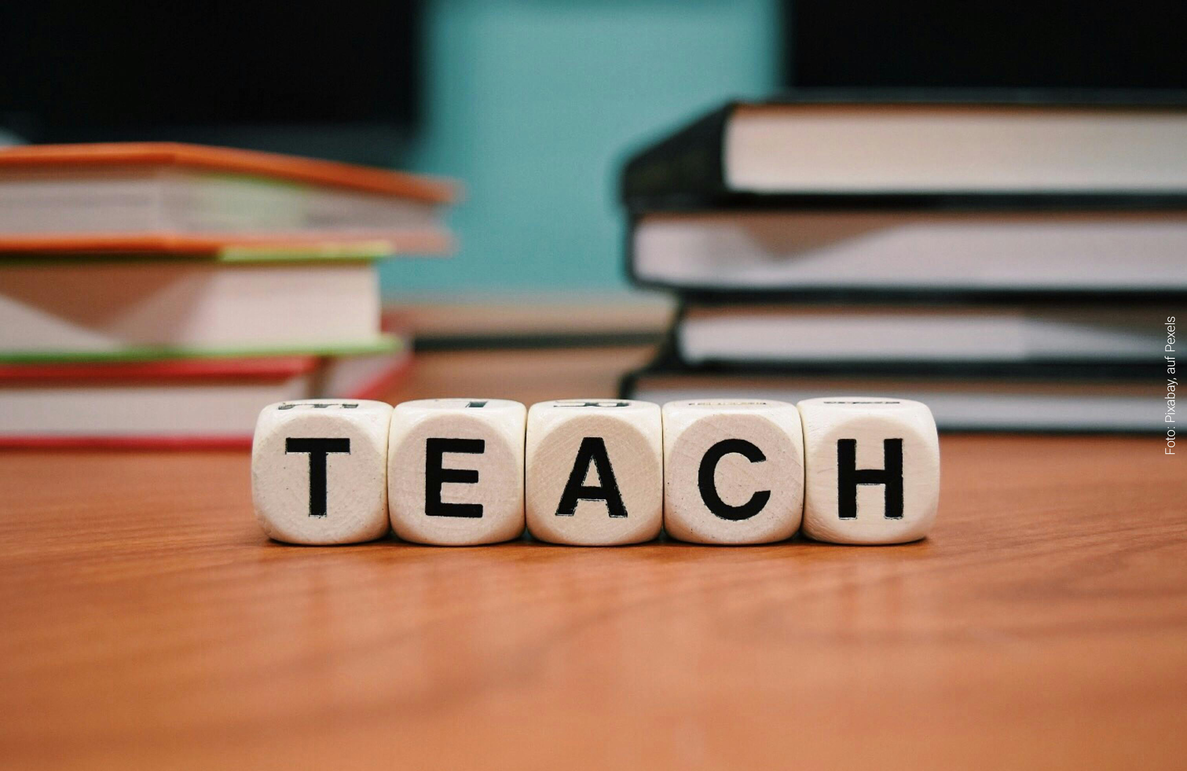 Würfel mit den Buchstaben "Teach" liegen vor ein paar Schulbüchern