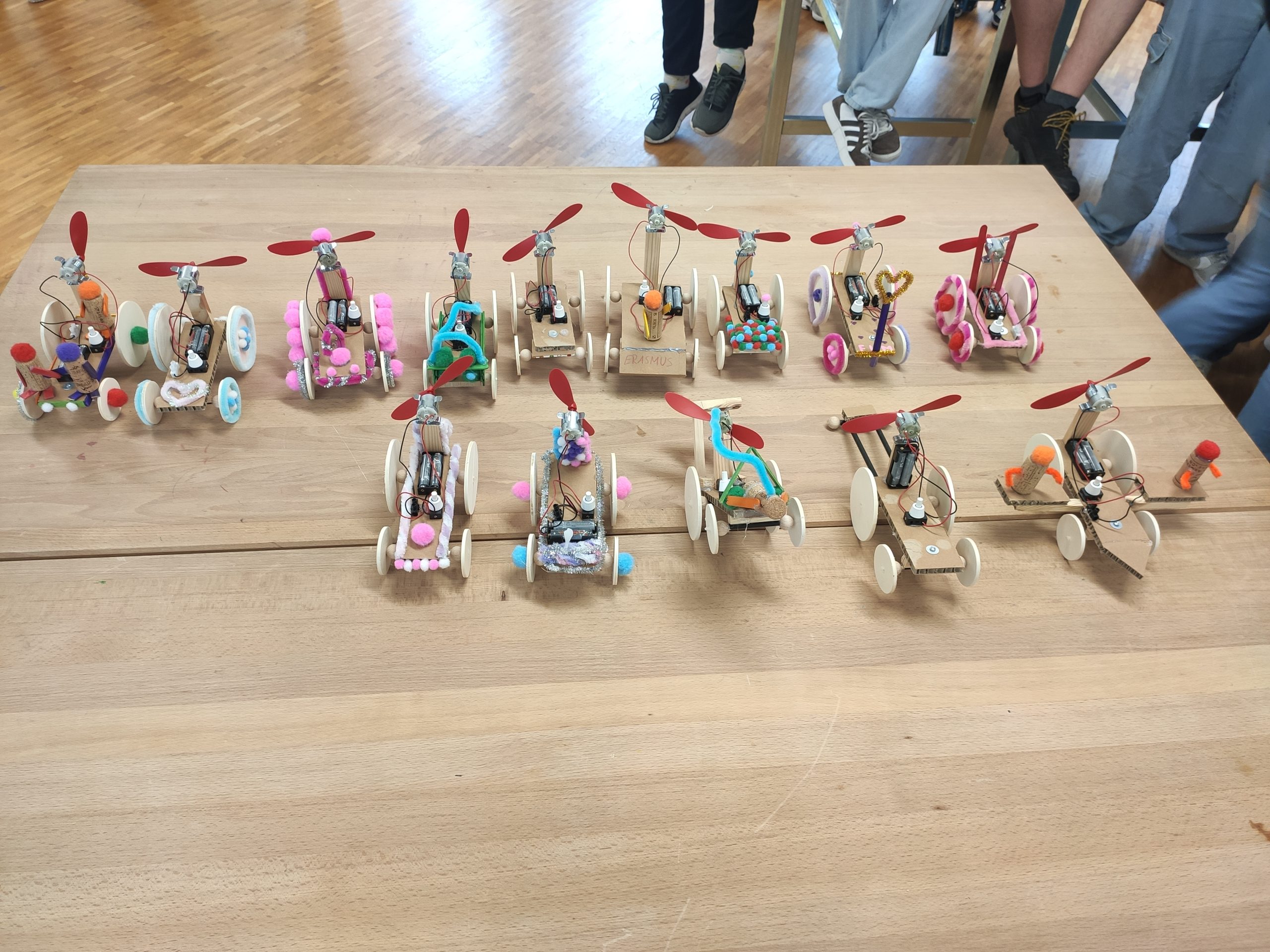Mehrere selbstgebaute kleine Fahrzeuge aus Holz mit Propellern und bunten Dekorationen stehen auf einem Tisch.