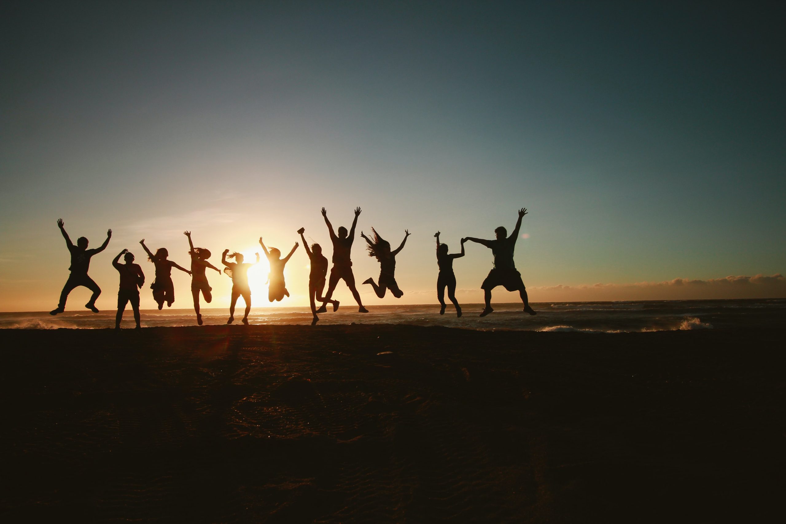 Junge Menschen springen am Strand beim Sonnenuntergang