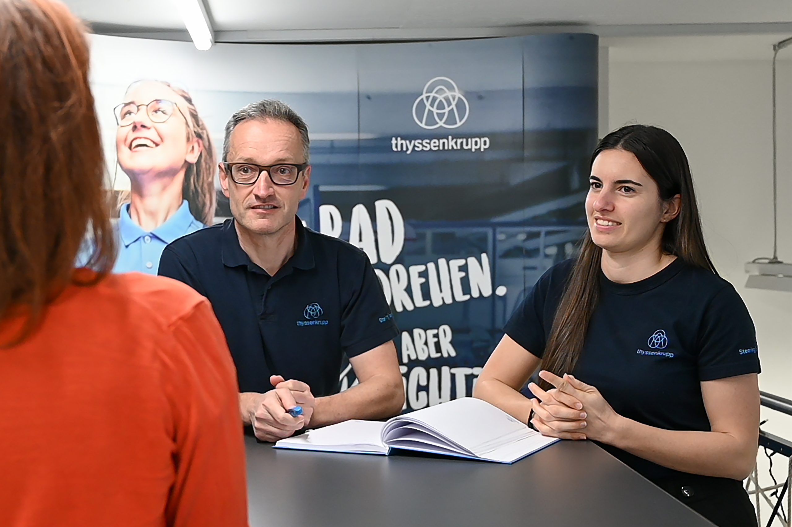 Drei Personen stehen an einem Tisch und führen ein Interview